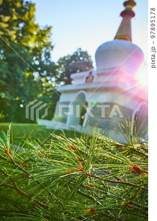 Blurry Tibetan Mongolian Buddhist Chorten shrine in background with solar flares and dewy pine needles in focus Blurry Tibetan Mongolian Buddhist Chorten shrine in background with solar flares and dewy pine needles in focus 97895178