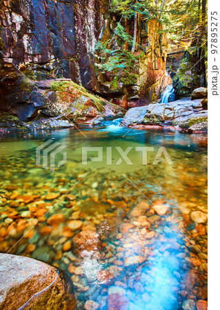 Clear river water with small rocks and canyon with waterfall in background 97895275