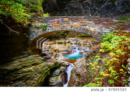Beautiful stone arch walking bridge over gorge and river with blue waters and waterfalls during fall 97895565