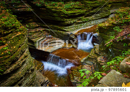 Beautiful tiers of waterfalls on river in deep canyon with mossy rocks and fall leaves 97895601