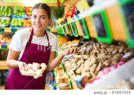 Happy young female seller puttingginger on shelves in grocery shop 97897939