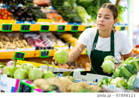 Focused female seller lay out round bottlegourd vegetable on counter in supermarket Focused female seller lay out round bottlegourd vegetable on counter in supermarket 97898123