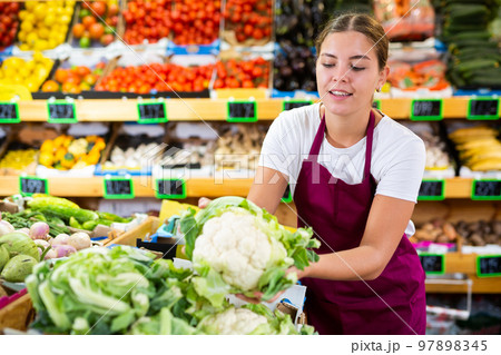 Friendly young seller woman in apron demonstrating cauliflower in shop Friendly young seller woman in apron demonstrating cauliflower in shop 97898345
