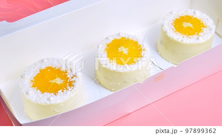 Small cakes with orange and coconut shavings in a box. 97899362