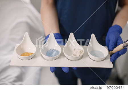 Close up of four different cosmetic cream jars. Cosmetologist holding moisturizing revitalizing creme lotions and other masks before applying on skin. Concept of treating yourself. 97900424