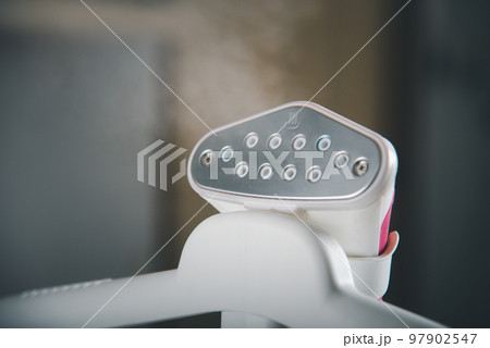 Close up of electric hand steam generator while it's hot on the ironing board place for clothes at house, Household and home equipment for housework, concept of linen care Close up of electric hand steam generator while it's hot on the ironing board place for clothes at house, Household and home equipment for housework, concept of linen care 97902547