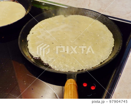 Cooking pancakes. Traditional russian blin on a cast-iron frying pan. Maslenitsa is an Eastern Slavic traditional holiday, celebrated during the week before the Great Lent. Cooking pancakes. Traditional russian blin on a cast-iron frying pan. Maslenitsa is an Eastern Slavic traditional holiday, celebrated during the week before the Great Lent. 97904745