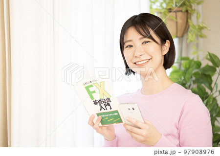 投資の本とスマートフォンを持つ女性 投資の本とスマートフォンを持つ女性 97908976