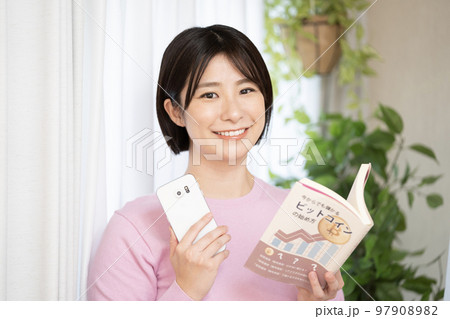 投資の本とスマートフォンを持つ女性 投資の本とスマートフォンを持つ女性 97908982