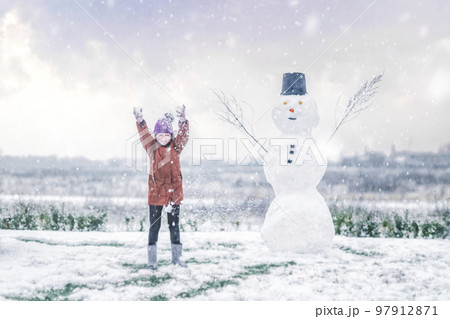 Girl cheering with a snowman in the snow 97912871