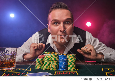 Wealthy man is posing at a poker table with chips and a glass of whiskey on it at a casino. Wealthy man is posing at a poker table with chips and a glass of whiskey on it at a casino. 97913241