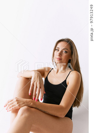 Beautiful woman with long hair sitting, posing in black underwear over grey studio background. Femininity, self-care Beautiful woman with long hair sitting, posing in black underwear over grey studio background. Femininity, self-care 97913249