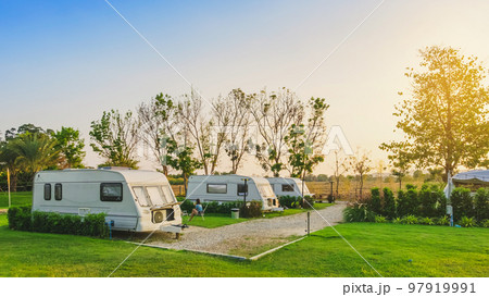 Cozy retro travel trailer Caravan on green grass before sunset near riverside in peaceful countryside. Family vacation travel RV, holiday trip in motorhome. Outdoor and Recreational Vehicles Theme. 97919991