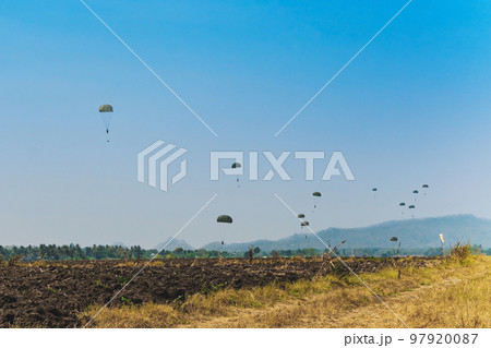 Army cadet paratroopers in military uniform landing on field. Skydiver paratrooper in parachute dome lands in the set area to land situated in the field among the soil. Military parachuting training. 97920087