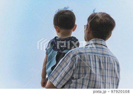 Back view of happiness Asian grandfather holding grandson with cloud and sky in background. Family stand to looking at beautiful sky together. Joy of outdoor living together. Happy family Back view of happiness Asian grandfather holding grandson with cloud and sky in background. Family stand to looking at beautiful sky together. Joy of outdoor living together. Happy family 97920108