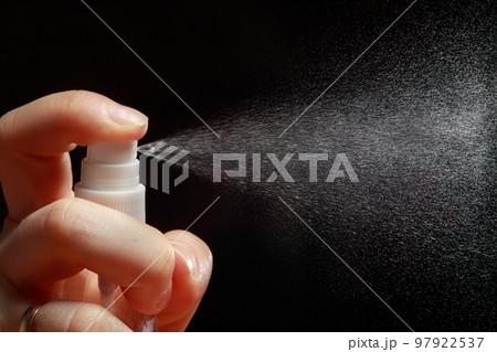 Man sprinkles a spray of perfume or sanitizer on a black background. Water spray or insecticide against insects or pests Man sprinkles a spray of perfume or sanitizer on a black background. Water spray or insecticide against insects or pests 97922537