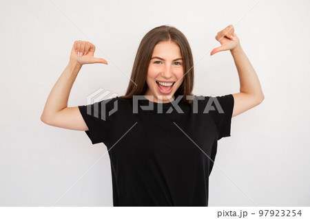 Portrait of excited young woman pointing thumbs at herself 97923254