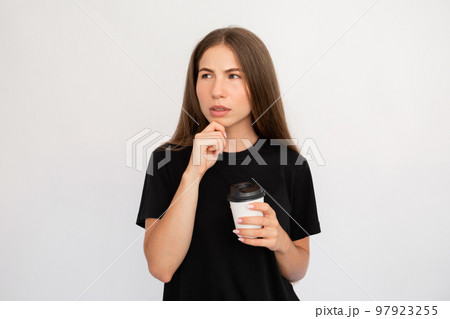 Portrait of doubtful young woman holding coffee cup Portrait of doubtful young woman holding coffee cup 97923255