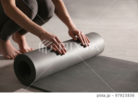 Woman rolling yoga mat in studio, closeup 97923836