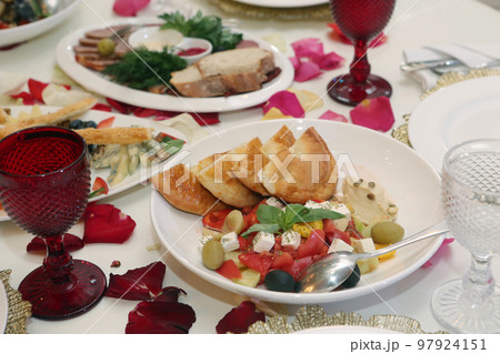 greek salad with tomato, olives, green, feta cheese and bread with wine glasses and rose petals 97924151