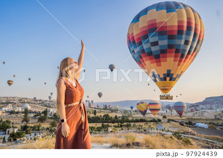 Tourist woman looking at hot air balloons in Cappadocia, Turkey. Happy Travel in Turkey concept. Woman on a mountain top enjoying wonderful view 97924439