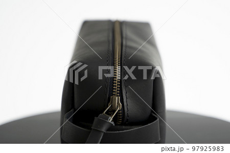 Close up black leather classic mens cosmetic bag with a metal gold zip on a black chair with a white background. 97925983