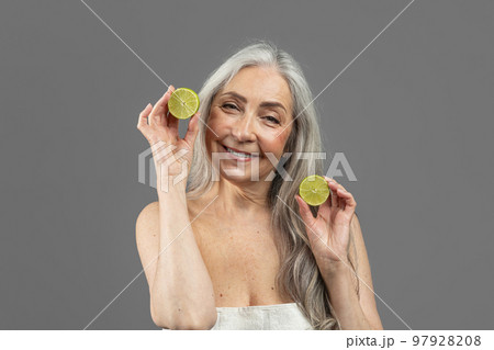 Smiling old caucasian lady with gray hair hold pieces of lemons, has fun, isolated on gray background, studio Smiling old caucasian lady with gray hair hold pieces of lemons, has fun, isolated on gray background, studio 97928208
