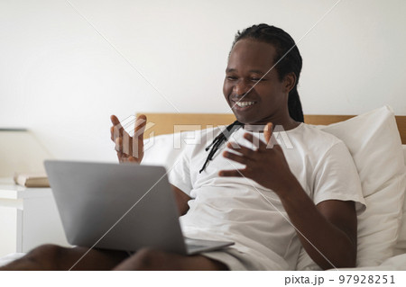 Video Call. Black Man Making Teleconference Via Laptop While Relaxing In Bed Video Call. Black Man Making Teleconference Via Laptop While Relaxing In Bed 97928251