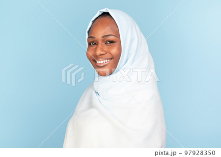 Portrait of beautiful black muslim woman in hijab posing on blue studio background, smiling at camera, copy space 97928350