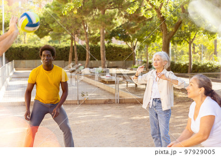 Joyful multiracial group of mature adult people playing volleyball game outdoors 97929005