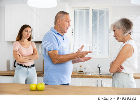 Quarrel between an elderly mother and an adult daughter in home kitchen. Father tries to calm everyone Quarrel between an elderly mother and an adult daughter in home kitchen. Father tries to calm everyone 97929232