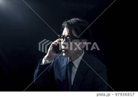 暗い部屋でスマートフォンで電話をかけているスーツを着たビジネスマンの男性 暗い部屋でスマートフォンで電話をかけているスーツを着たビジネスマンの男性 97936817