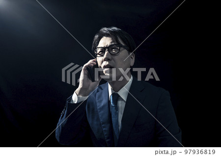 暗い部屋でスマートフォンで電話をかけているスーツを着たビジネスマンの男性 暗い部屋でスマートフォンで電話をかけているスーツを着たビジネスマンの男性 97936819