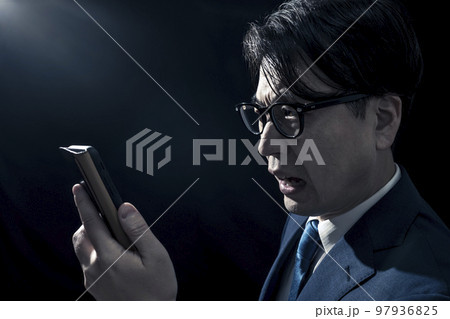 暗い部屋でスマートフォンの画面を見ているビジネスパーソン 暗い部屋でスマートフォンの画面を見ているビジネスパーソン 97936825