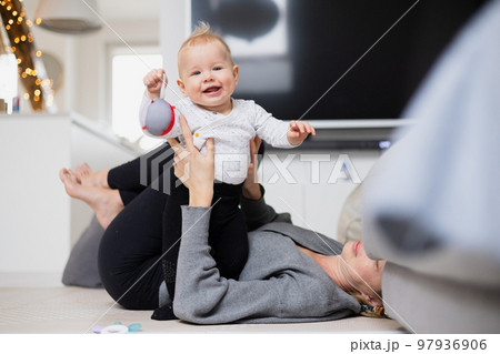 Happy family moments. Mother lying comfortably on children's mat playing with her baby boy watching and suppervising his first steps. Positive human emotions, feelings, joy 97936906