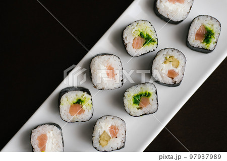 Rolls with cheese and salmon on a white rectangular plate on a dark background. 97937989