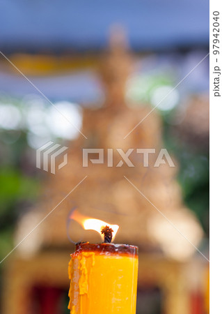 Candlelight burning in front of Buddha statue. Focus on candle frame, buddha blured in background 97942040
