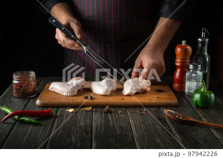 The chef prepares chicken nugget with raw chicken wings in the kitchen. Space for advertising on a dark background The chef prepares chicken nugget with raw chicken wings in the kitchen. Space for advertising on a dark background 97942226
