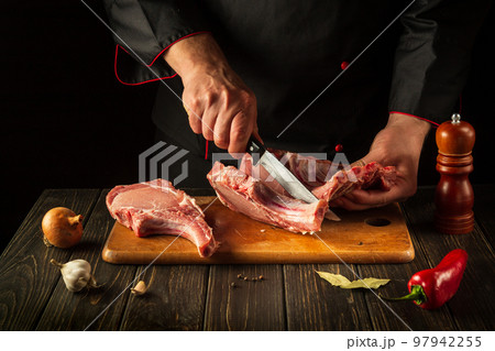 Butcher cuts raw ribs on a cutting board before grilling. European cuisine. Meat dish idea for a hotel 97942255