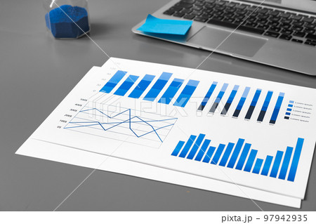 Printed graphs and laptop on dark gray surface Printed graphs and laptop on dark gray surface 97942935