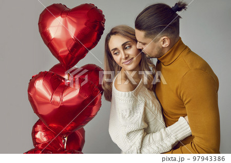 Young, beautiful, in love couple in a romantic atmosphere hugging among balloons in the shape of a heart. 97943386