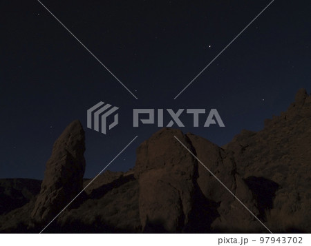 Long exposure night shot of Roques de Garcia volcanic rock formation at El Teide national park, night winter sky with stars on dark blue. Tenerife Canary islands, Spain Long exposure night shot of Roques de Garcia volcanic rock formation at El Teide national park, night winter sky with stars on dark blue. Tenerife Canary islands, Spain 97943702