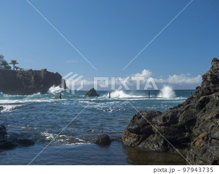 View of natural rock swimming pool Charco de Isla Cangrejo in the Atlantic Ocean in Los Gigantes, Tenerife, Canary islands, Spain. Sunny winter day. View of natural rock swimming pool Charco de Isla Cangrejo in the Atlantic Ocean in Los Gigantes, Tenerife, Canary islands, Spain. Sunny winter day. 97943735