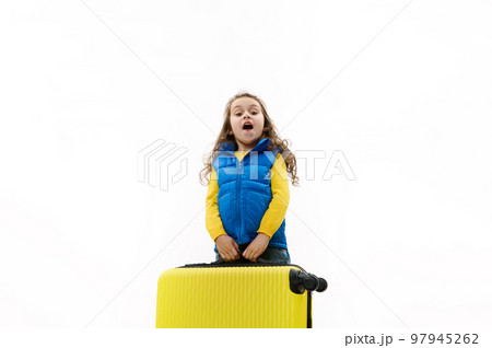 Caucasian beautiful little kid girl in blue jacket, going for weekend getaway, carrying a heavy yellow suitcase, isolated on white background. Travel. Trip. Journey. Air Flight. Copy advertising space Caucasian beautiful little kid girl in blue jacket, going for weekend getaway, carrying a heavy yellow suitcase, isolated on white background. Travel. Trip. Journey. Air Flight. Copy advertising space 97945262