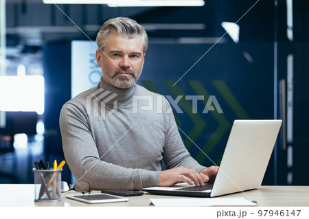 Portrait of serious gray haired boss, man looking at camera thinking, mature businessman inside office working at desk using laptop at work. Portrait of serious gray haired boss, man looking at camera thinking, mature businessman inside office working at desk using laptop at work. 97946147
