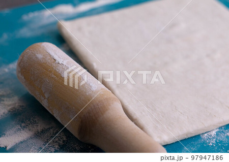 A piece of puff pastry and a wooden rolling pin on a turquoise board 97947186