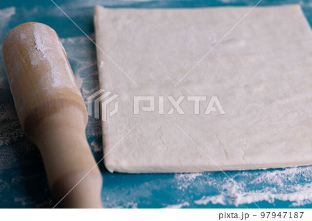 A piece of puff pastry and a wooden rolling pin on a turquoise board 97947187