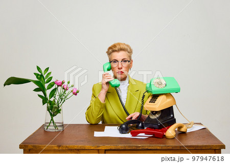 Lady boss. Creative portrait of fashionable middle age woman in vintage style clothes among retro interior objects over light background. 97947618