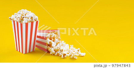 Two red white striped carton buckets with tasty cheese popcorn, isolated on yellow background 97947843