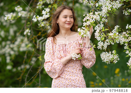A girl in a pink dress stands near a white tree with flowers looks away and smiles A girl in a pink dress stands near a white tree with flowers looks away and smiles 97948818